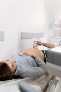 A pregnant woman is getting an ultra sound scan at a doctor's office. She looks at the monitor while the female doctor is scanning the abdomen.