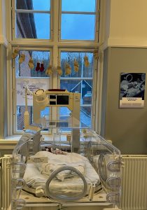 Incubator featuring a knitted line with small baby socks and a poster about World Prematurity Day.